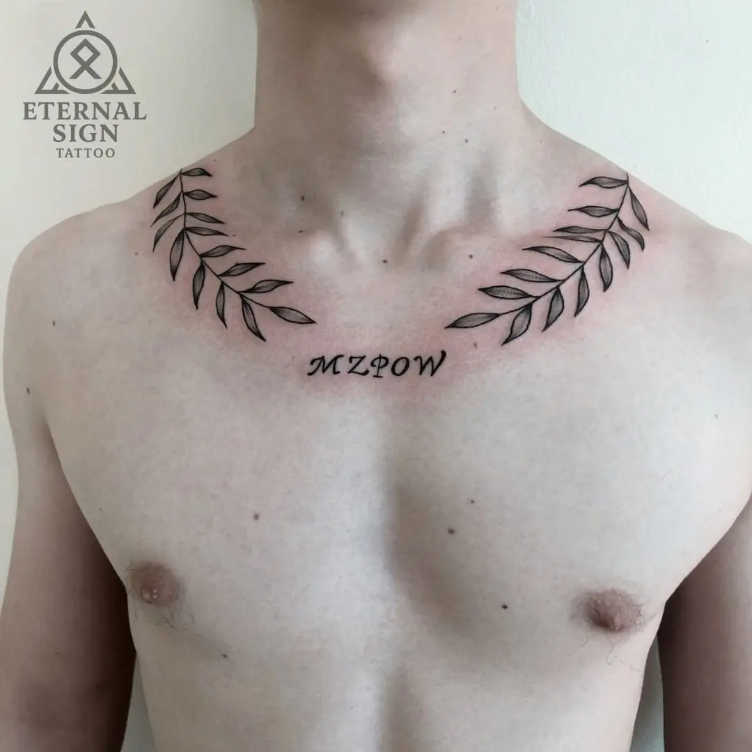 Symmetrisk krans av blad og monogram 'MZΦOW' under kragebein i minimalstisk finline-stil på brystet i Fredrikstad.