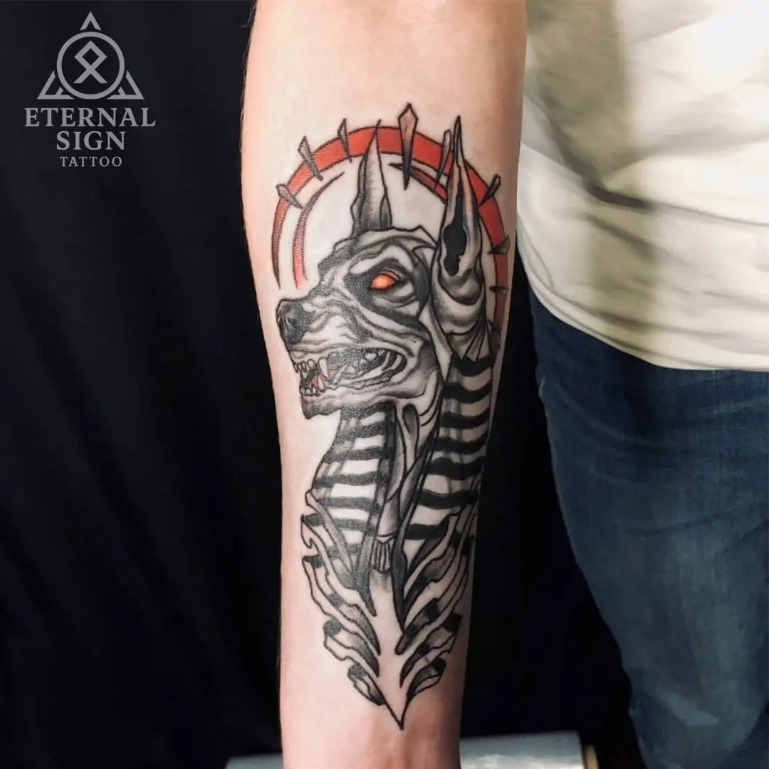Detaljert black & grey tatovering av Anubis-hodet med glødende røde øyne og rød taggete glorie på underarmen.