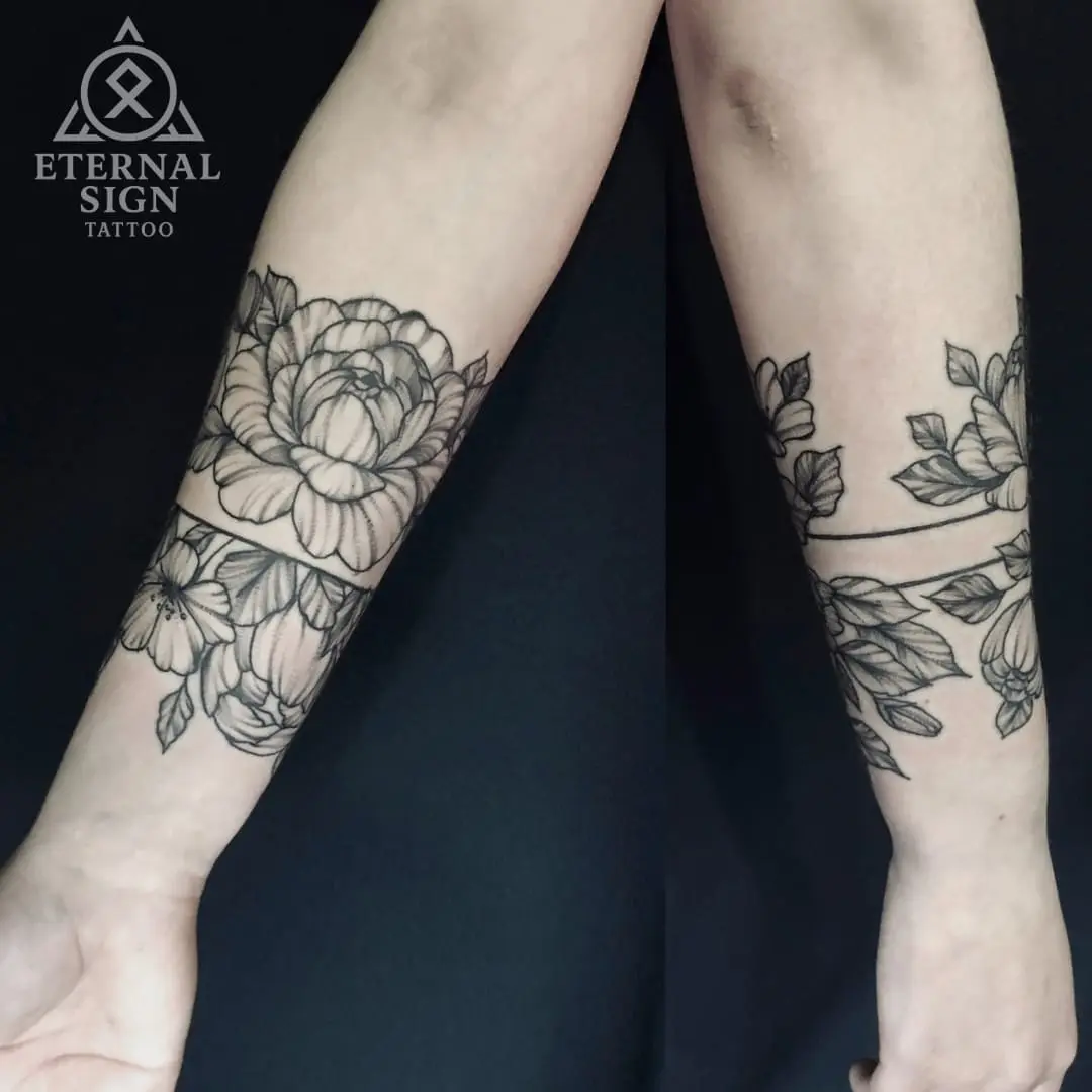 Detaljerte blackwork-blomstertatoveringer som danner bånd rundt begge underarmene med peoner og blader i Fredrikstad.