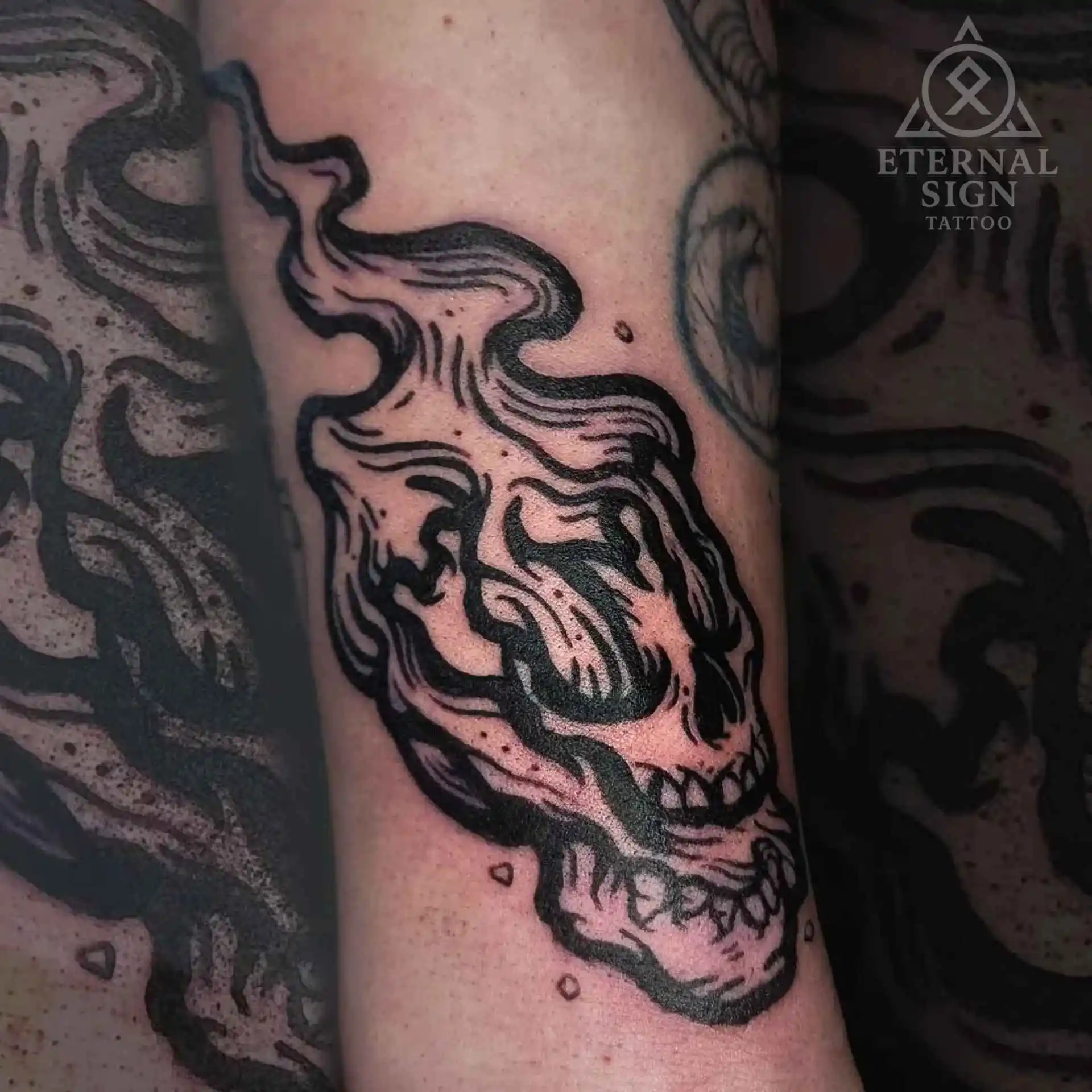 Abstrakt blackwork-tatovering av en stilisert skalleform som smelter i røyk eller væske.