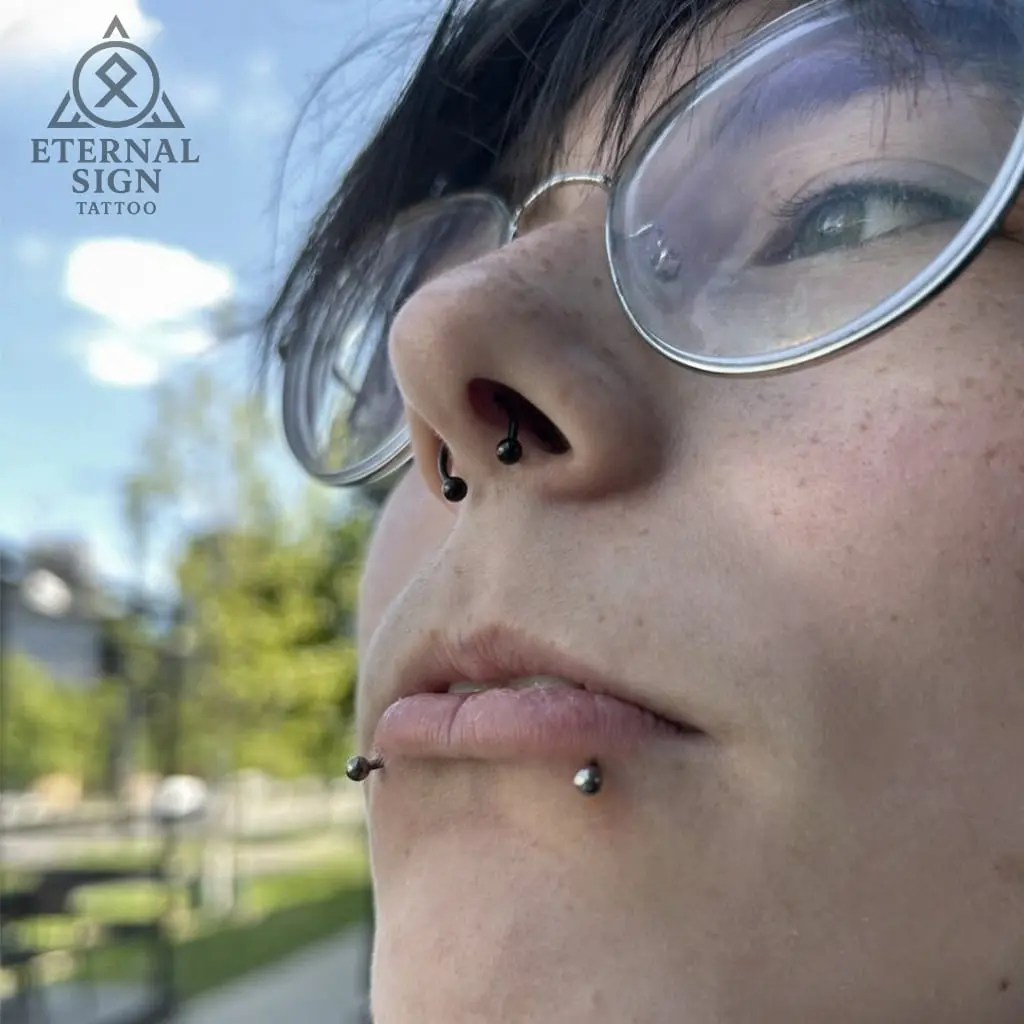 Septum piercing og labret piercing i underleppen – trendy ansiktspiercing med svart og sølv smykker